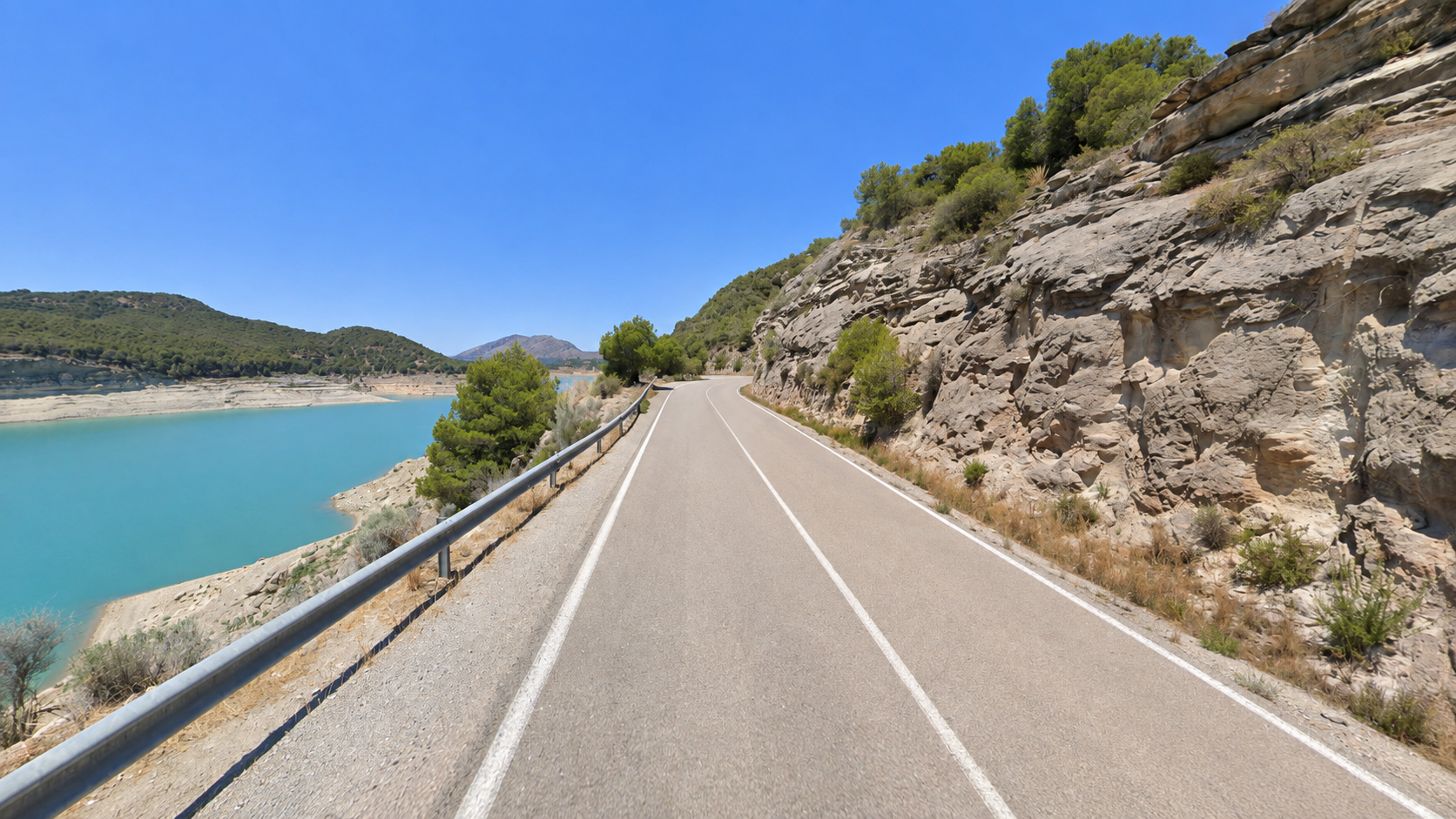 Empty road beside a blue reservoir near Granada